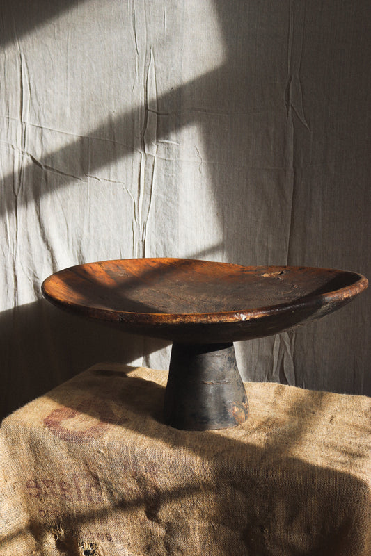 Wooden dish on a stand against a textured wall
