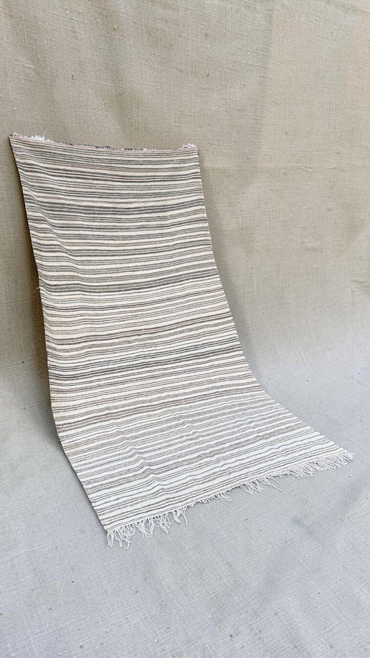 Angled view of the cream striped Moroccan textile and fringed ends