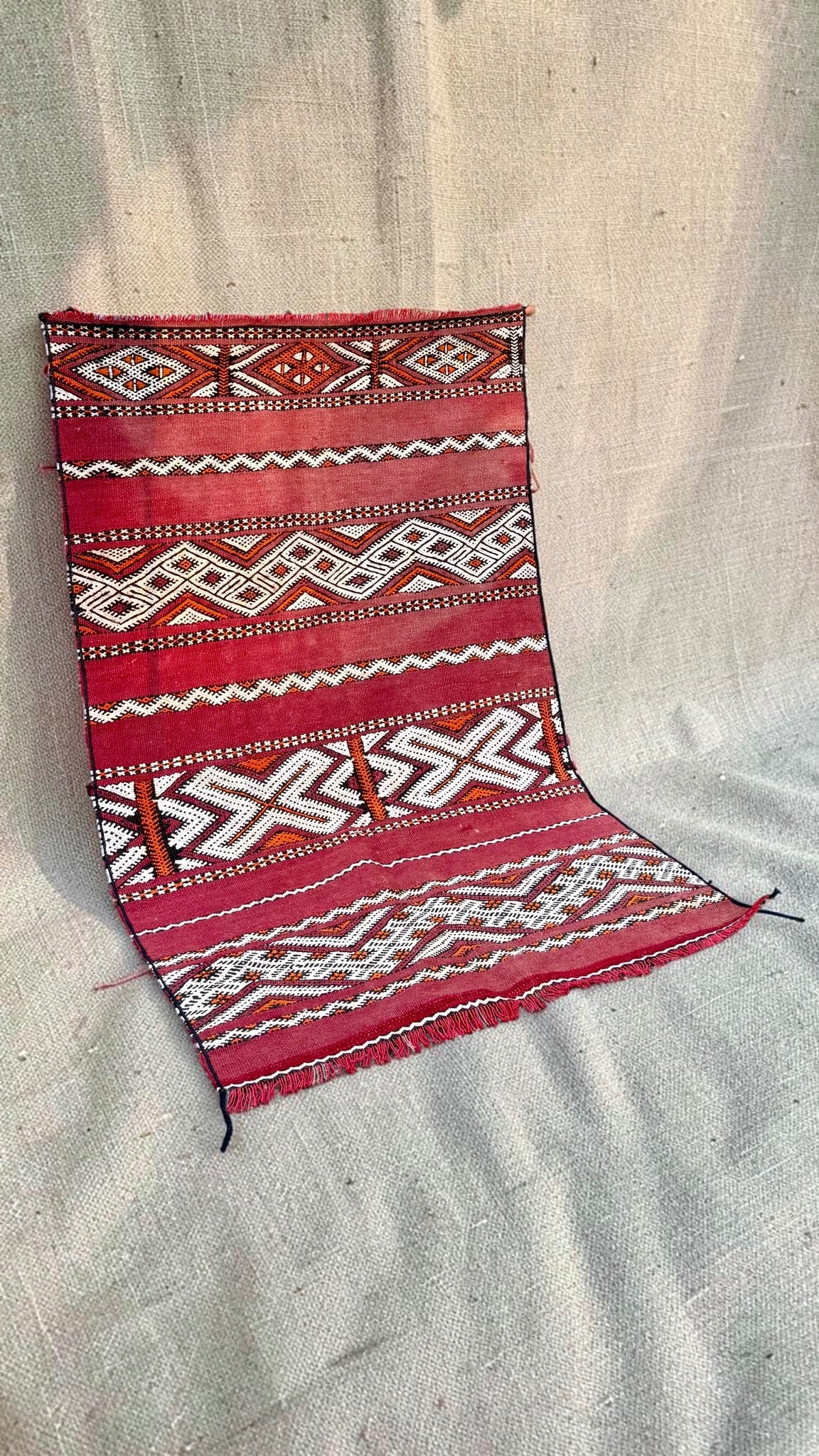 Angled view of the small red Moroccan Hanbel rug and short fringed ends