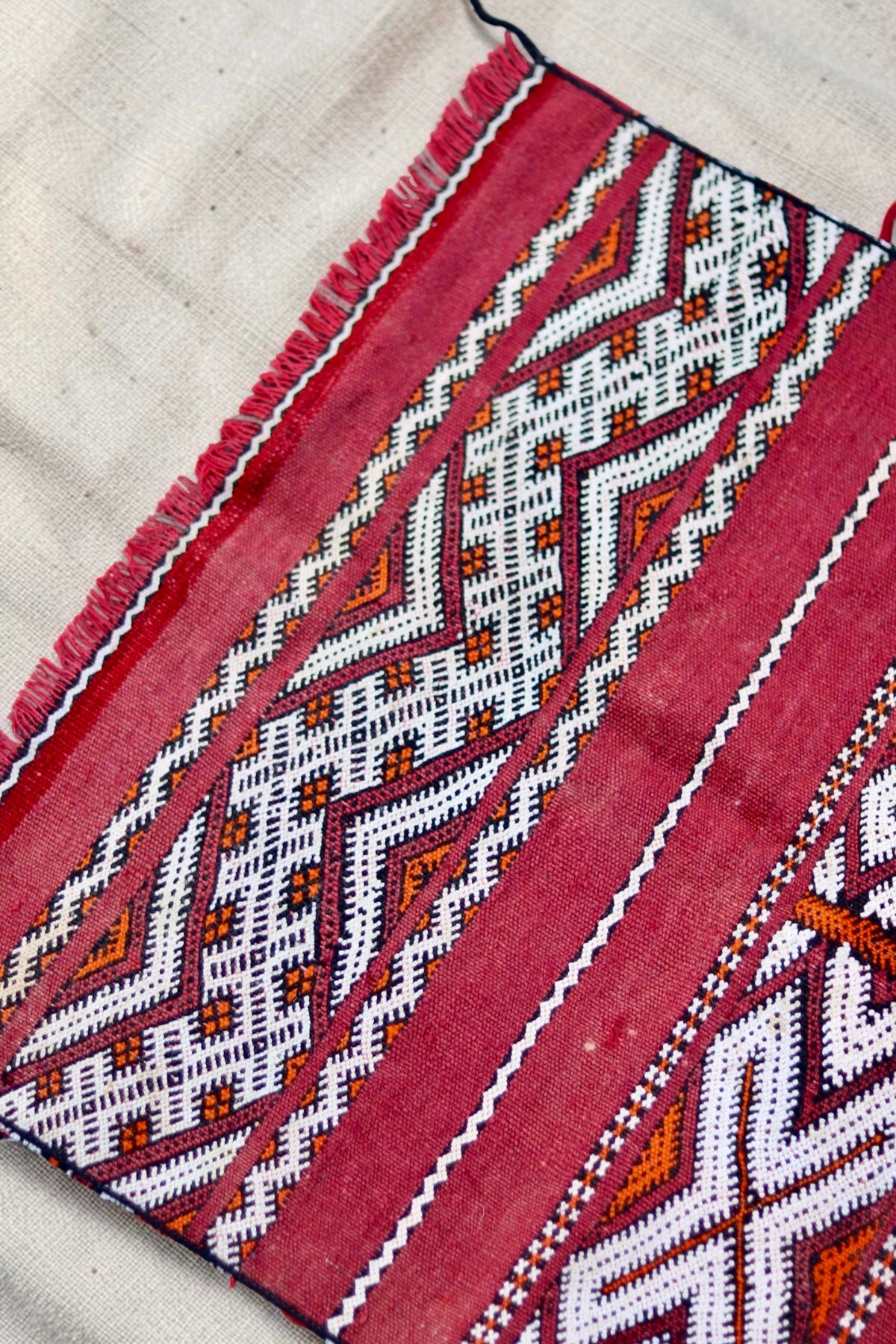Detail of the geometric pattern, red fringe and small pale marks in the vintage weave