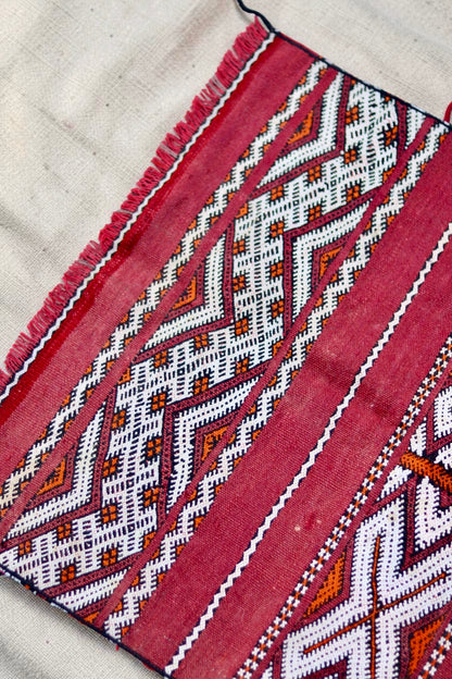 Detail of the geometric pattern, red fringe and small pale marks in the vintage weave