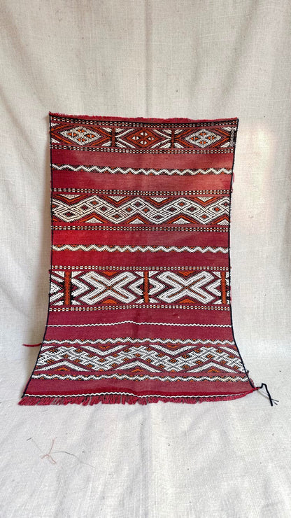 Small vintage Moroccan Hanbel rug with a faded red ground and cream, black and orange geometric bands