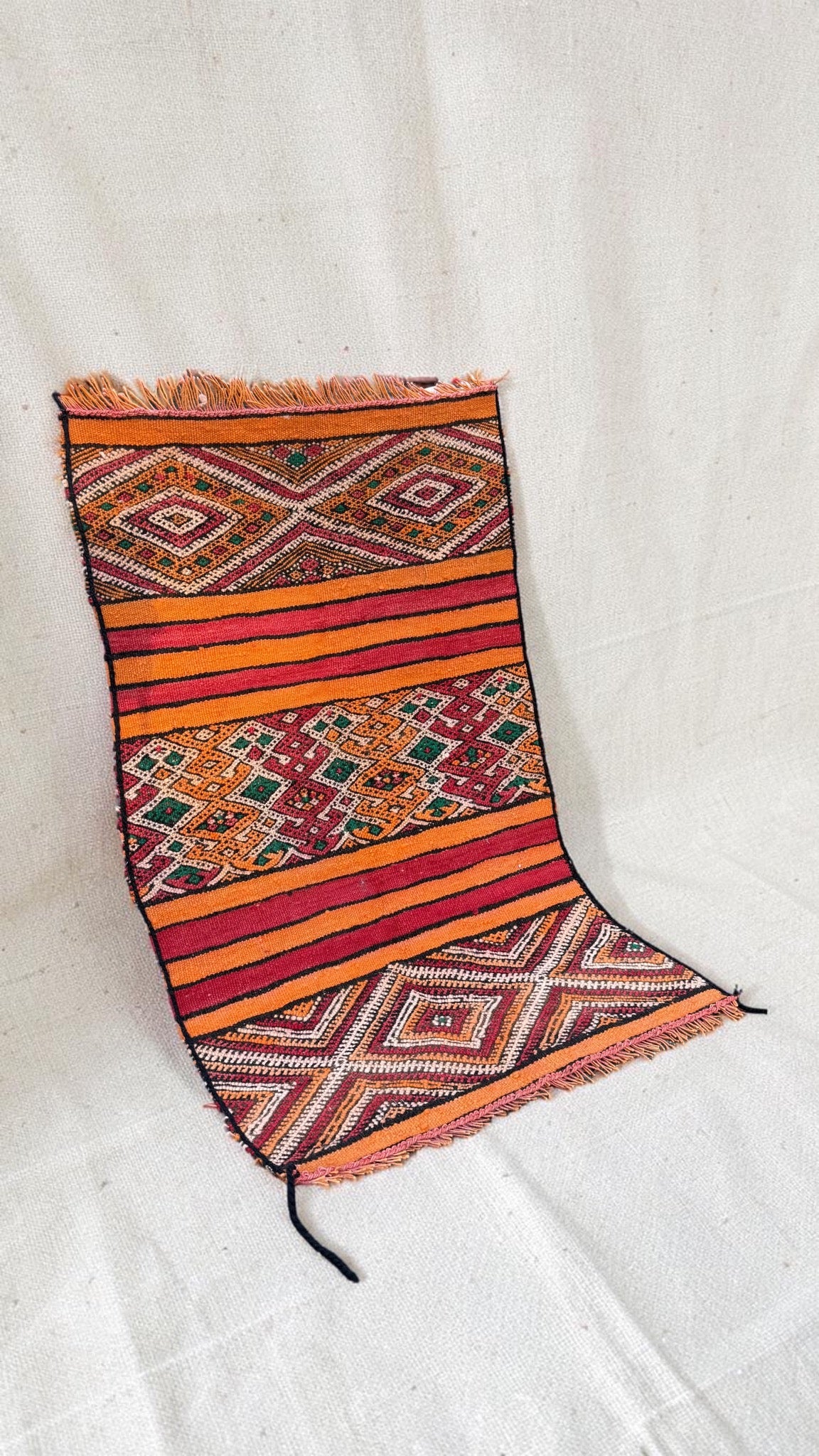 Angled view of the small orange and red Hanbel rug with short fringed ends