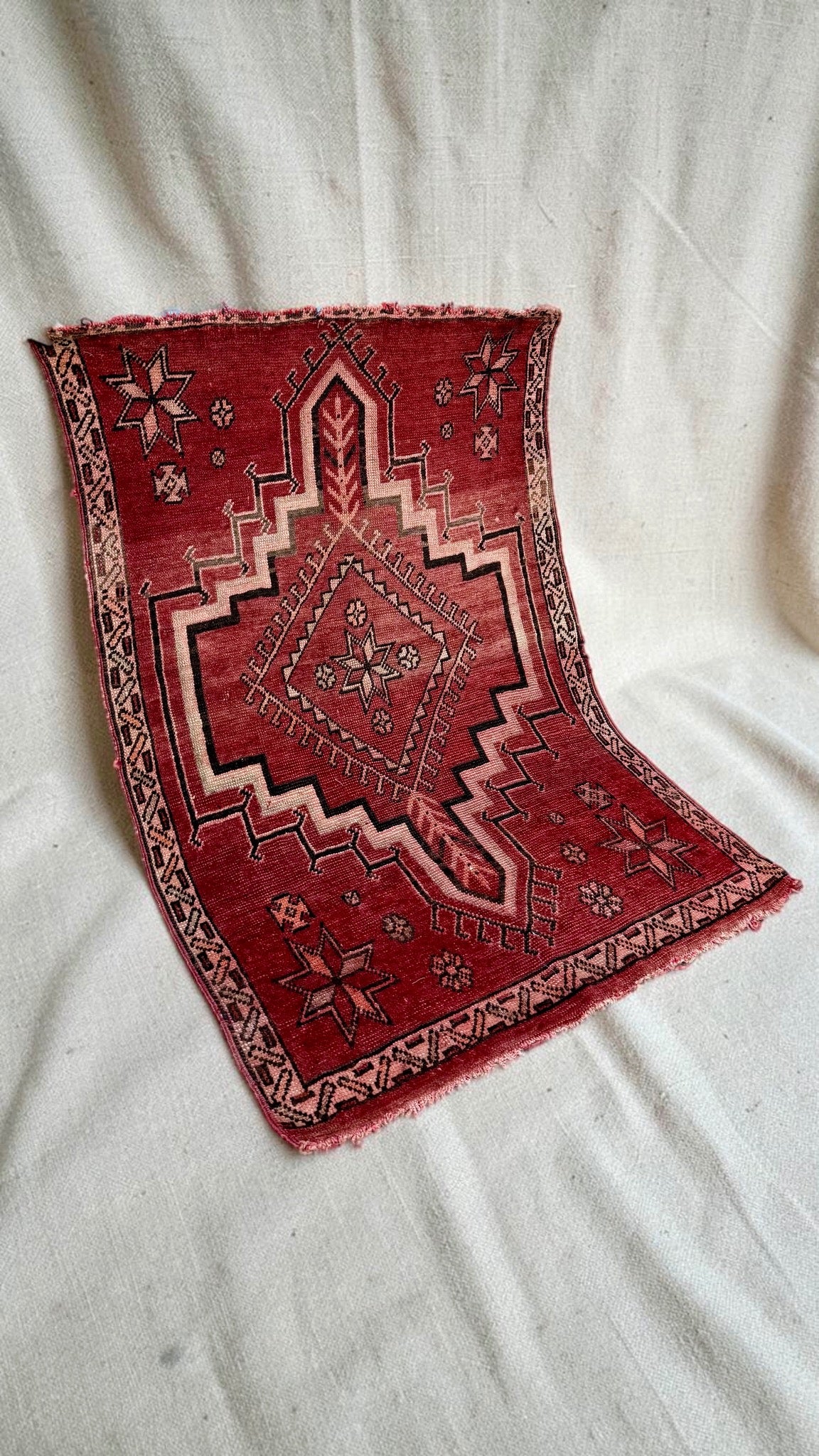 Angled view of the red and pink vintage rug showing the patterned border and worn ends