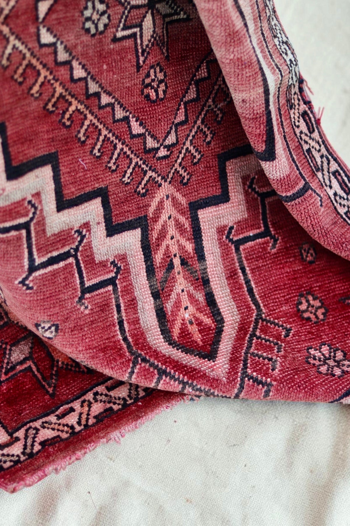 Folded detail of the faded red rug, pale pink medallion and dark outlines
