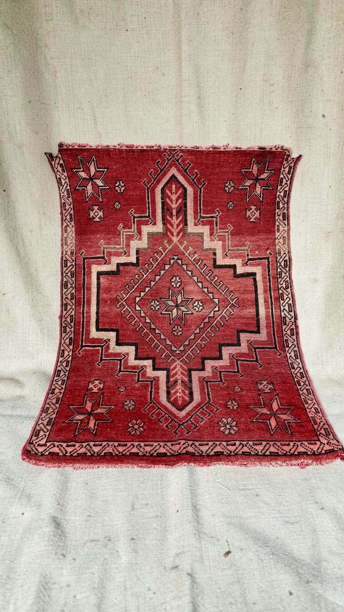 Small vintage Moroccan rug in faded red and pink with a stepped central medallion and star motifs
