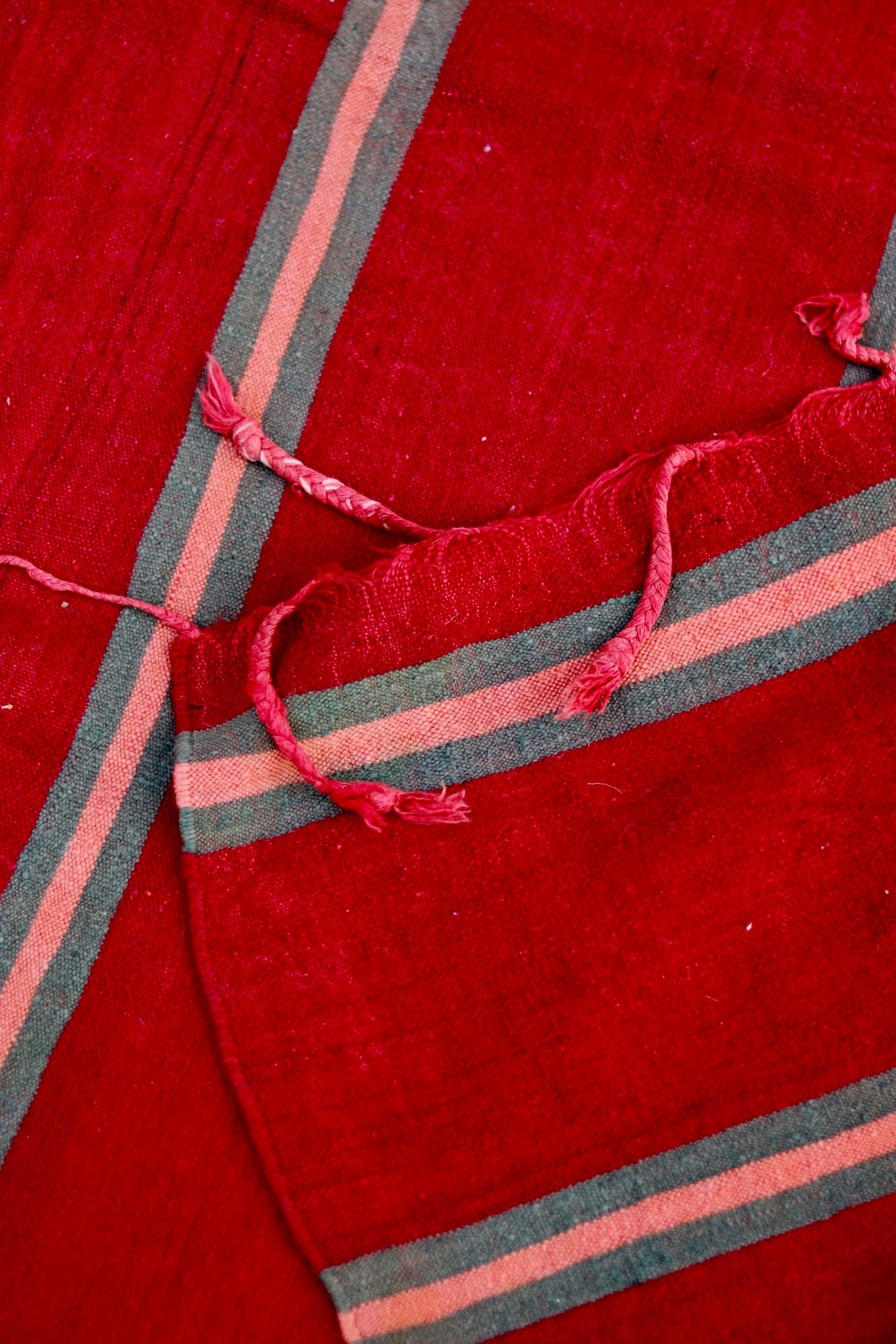 Folded ends of the vintage Moroccan flatweave showing red tassels