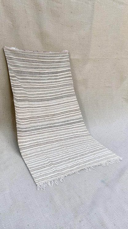 Angled view of the cream striped Moroccan textile and fringed ends