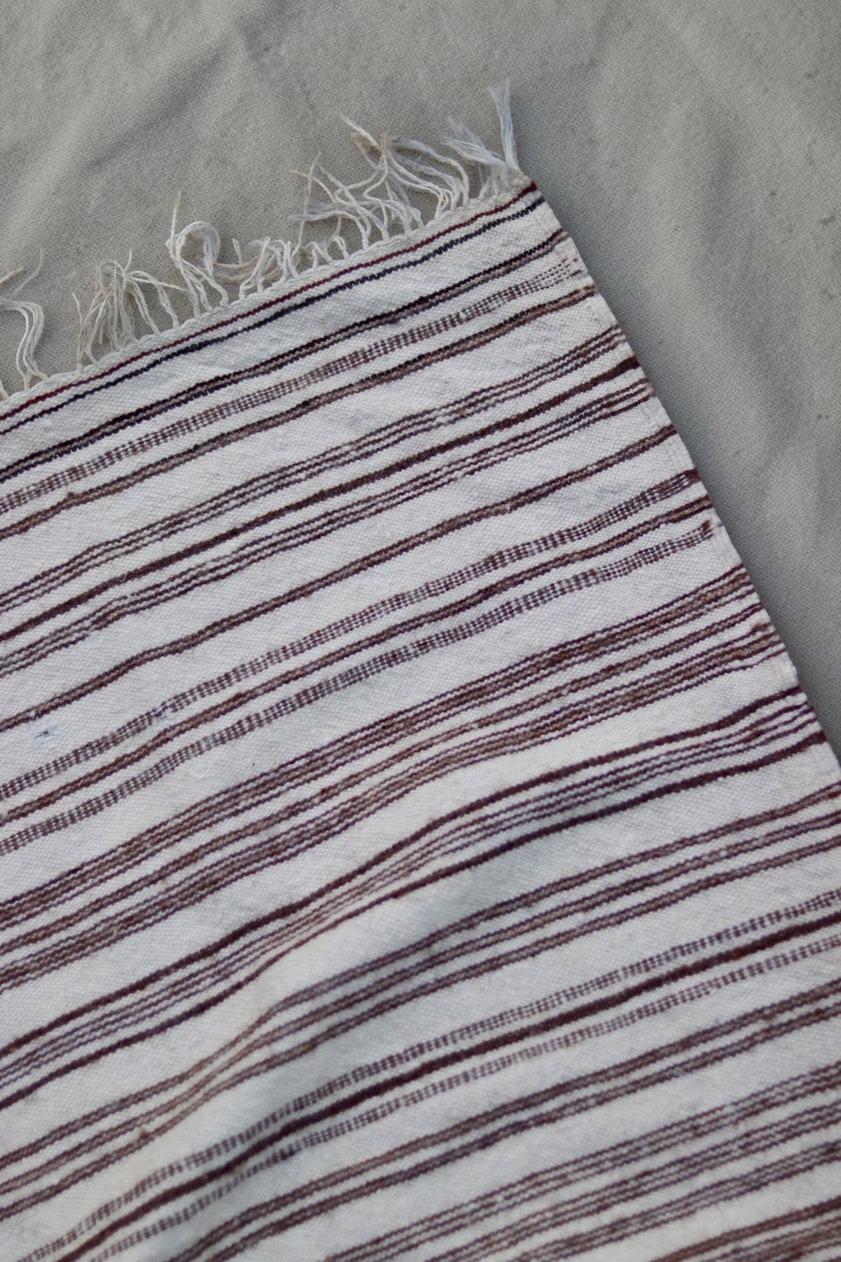 Corner and fringe detail showing fine brown stripes in the cream weave