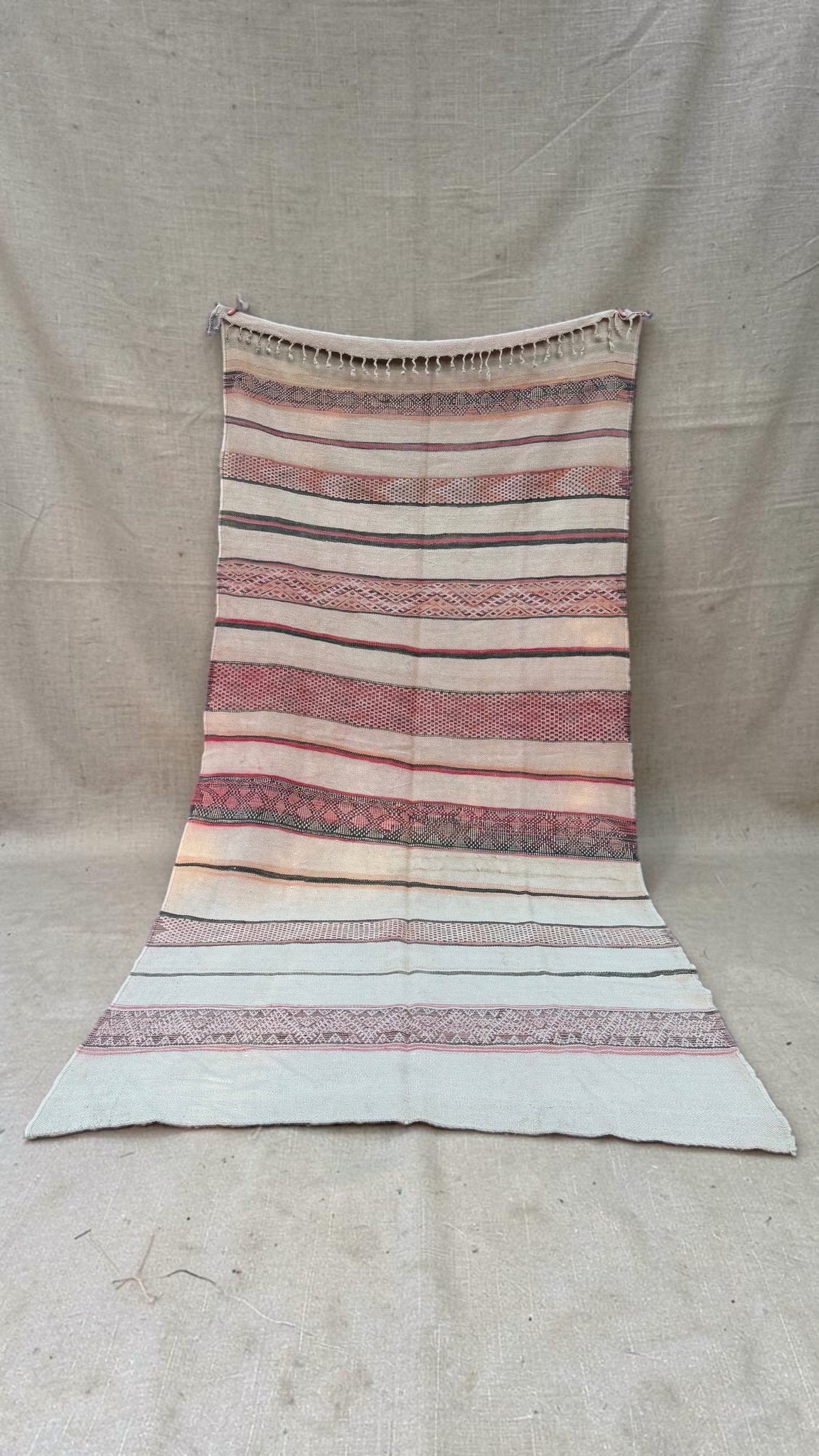 Full view of a vintage Moroccan Hanbel rug in cream, faded rose pink and charcoal with geometric bands