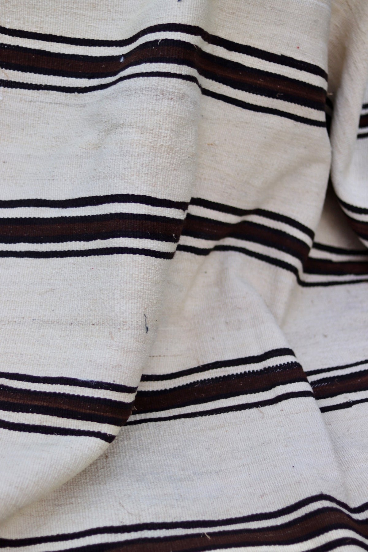 Folded detail showing the dense flatweave and cream ground with brown and charcoal stripes