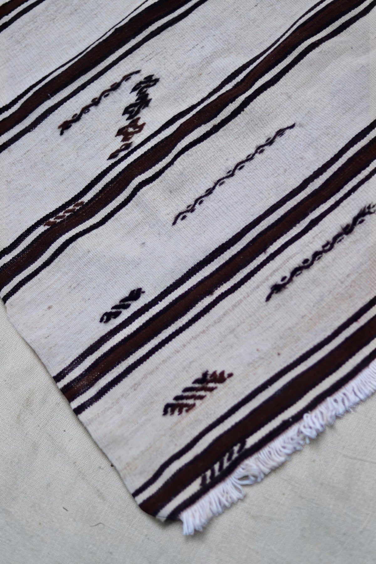 Small dark geometric motifs and striped bands near the fringed end